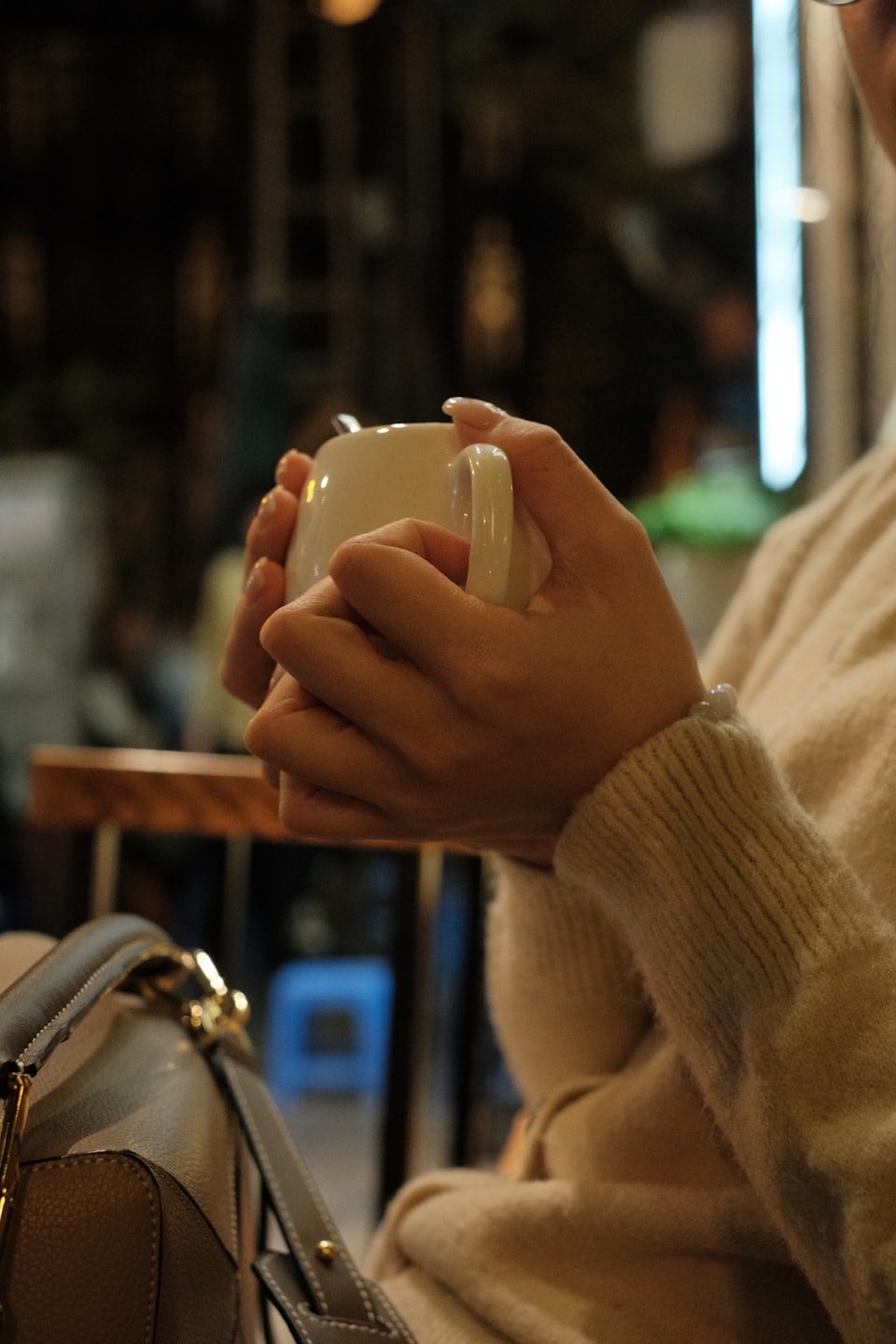 Hände in einem Strickpullover halten eine warme Keramiktasse.